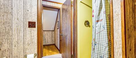 Un baño con puerta de madera, un perchero con un rollo de toallas de papel y una cortina de ducha estampada.