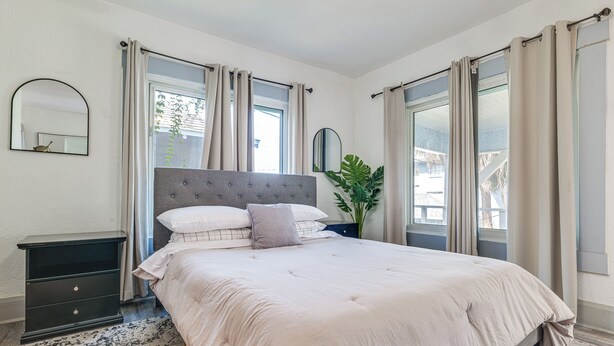 A bedroom with a large bed, a nightstand, a mirror, and a potted plant. - Walk to Winter Haven Hospital: Convenient Apt (Winter Haven)