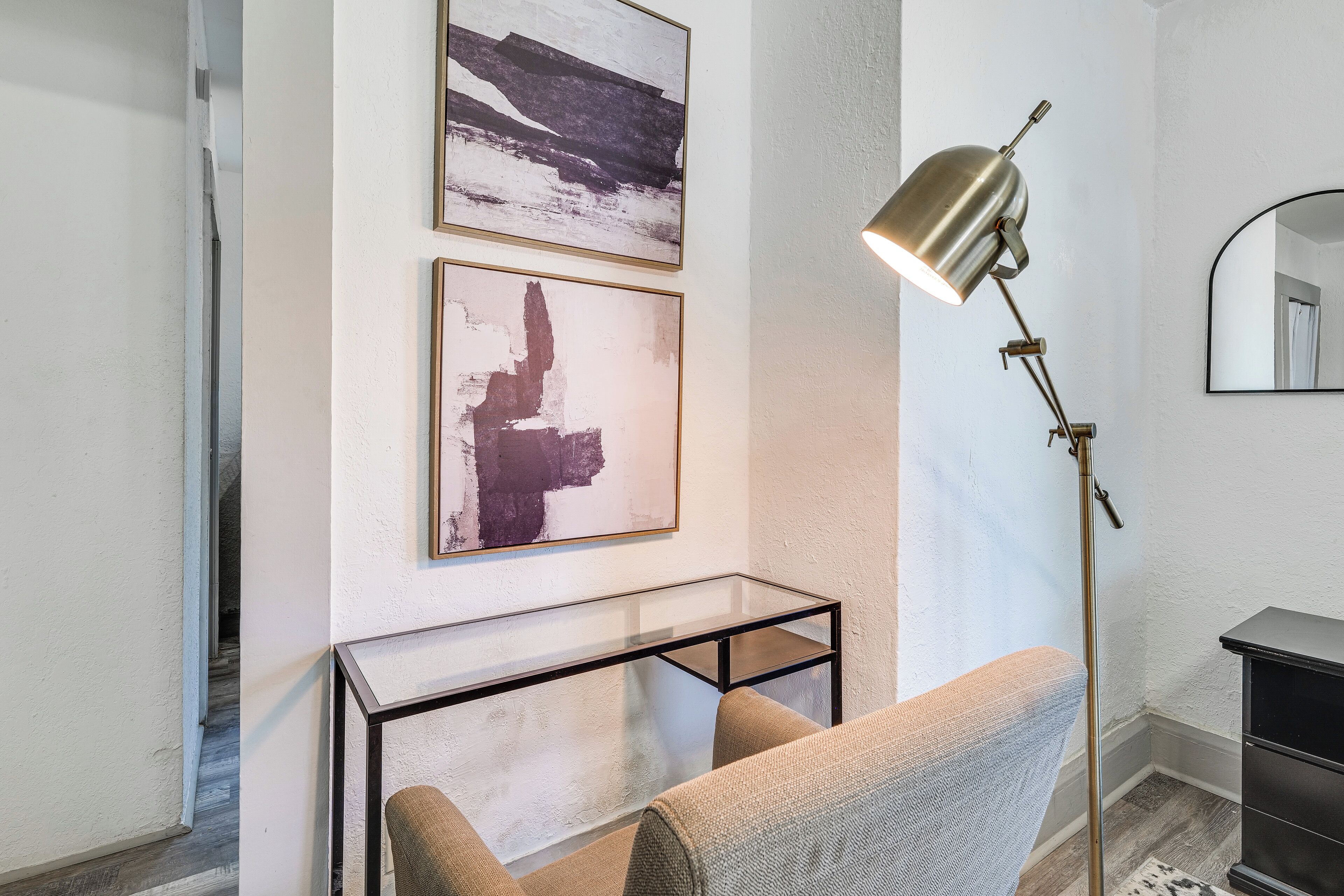Une pièce moderne avec une table basse en verre, un canapé, un lampadaire et des œuvres d’art abstraites accrochées au mur.