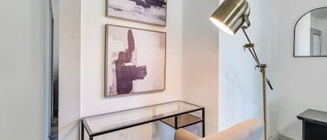 Une pièce moderne avec une table basse en verre, un canapé, un lampadaire et des œuvres d’art abstraites accrochées au mur.