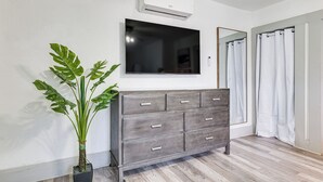 A modern room with a grey dresser, a large flat-screen TV mounted above it, a potted plant, and a shower area with white curtains. - Walk to Winter Haven Hospital: Convenient Apt (Winter Haven)