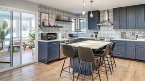 Une cuisine moderne avec des meubles de couleur bleu foncé, un îlot central doté de tabourets de bar et une grande fenêtre qui laisse entrer la lumière naturelle.