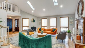 Un salon spacieux avec un canapé vert aux lignes arrondies, deux fauteuils orange, une table basse et une cheminée.