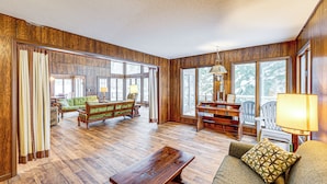 Ein geräumiges Wohnzimmer mit Holzböden, einem grünen Sofa, einem Couchtisch aus Holz und einem großen Fenster, das für natürliches Licht sorgt.