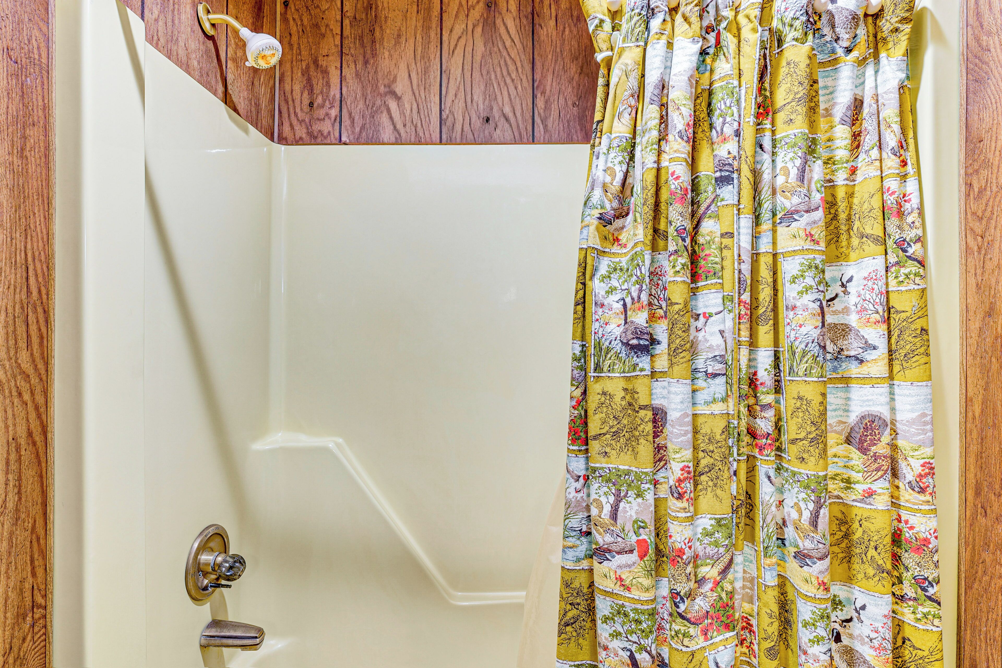 Une salle de bain avec une baignoire blanche, un lambris en bois et un rideau de douche à motifs floraux.