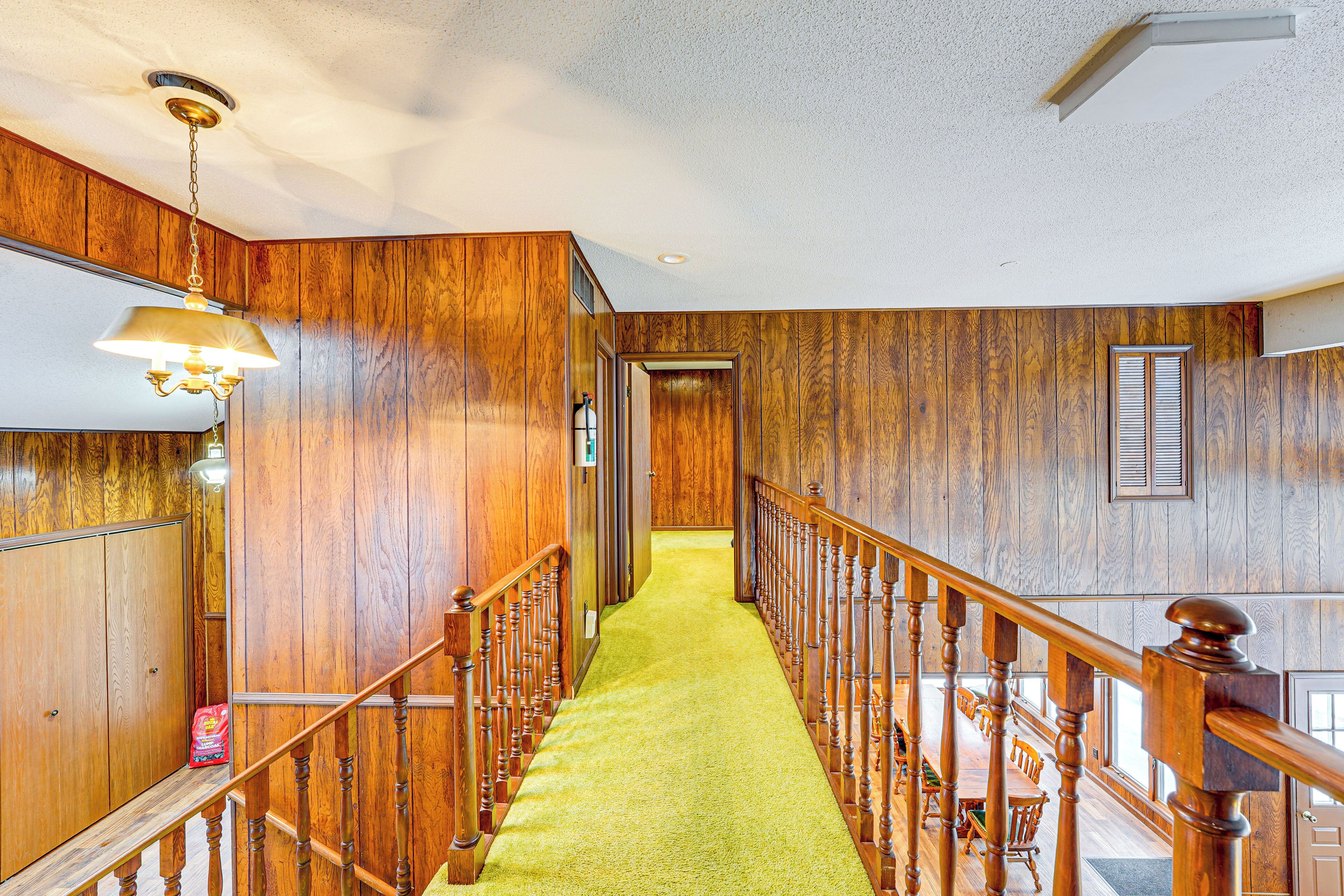 A wooden interior hallway with a green carpet, wooden railings, and a chandelier.