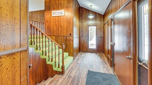 Eine Holztreppe mit grünem Teppich, einer Chandelier und einer Tür mit Fenster.