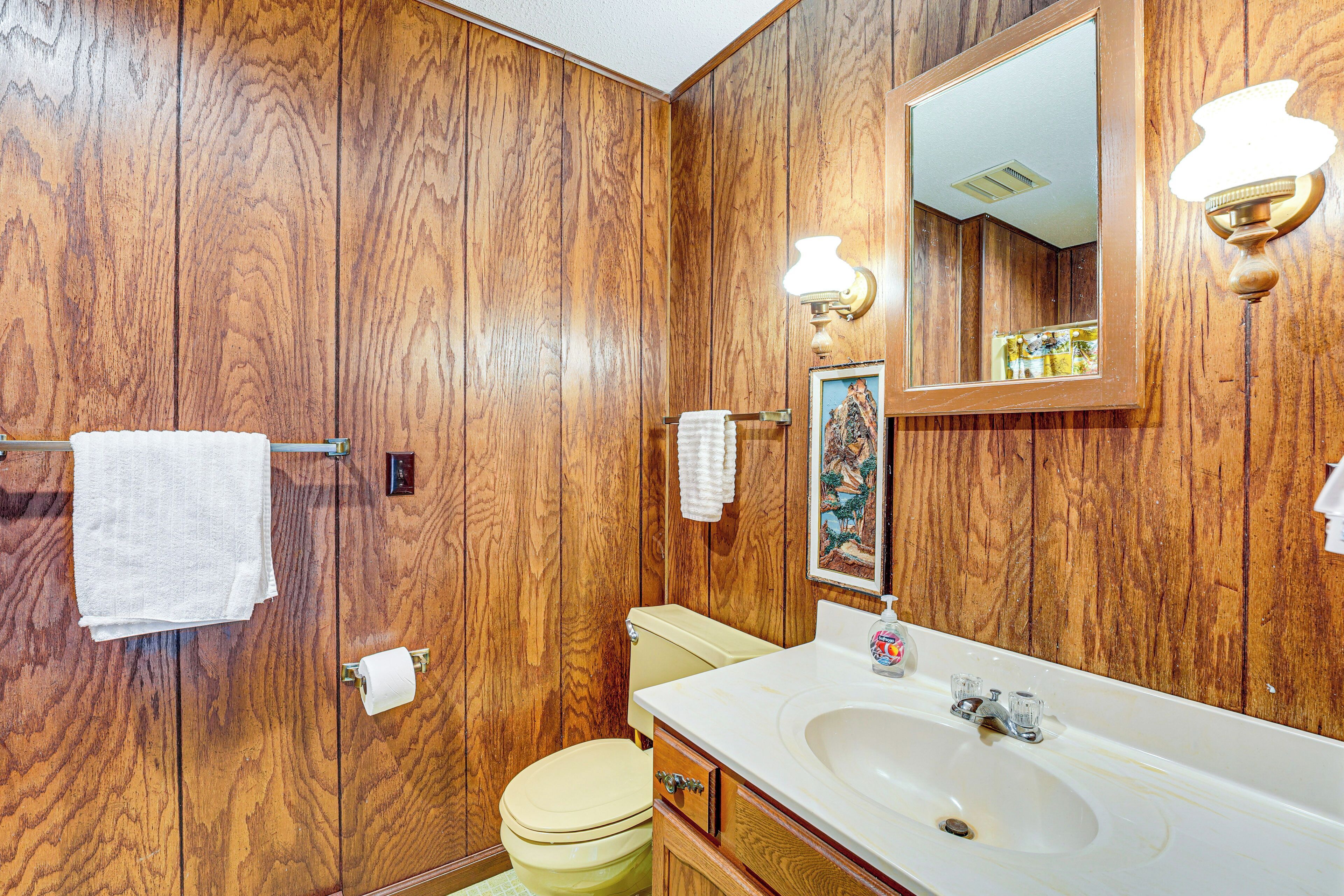 A wooden-paneled bathroom with a white sink, a toilet, and a mirror.