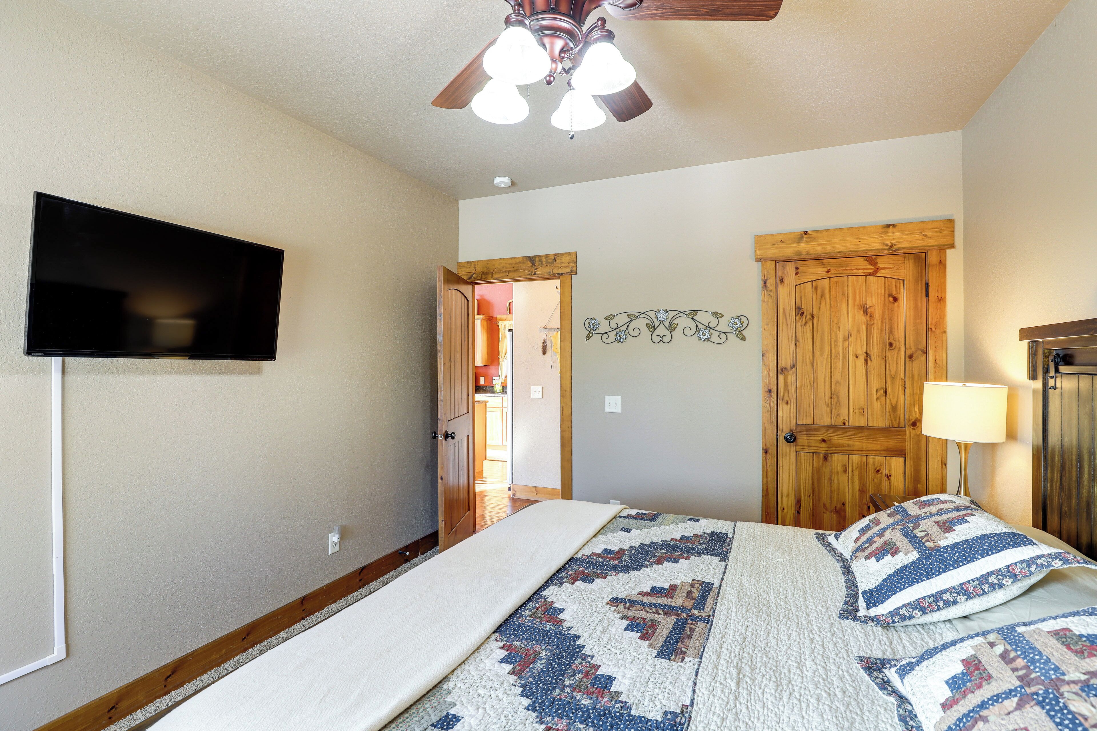 Un dormitorio con cama, ventilador de techo, televisor, puertas de madera y un pasillo que conduce a otra habitación.