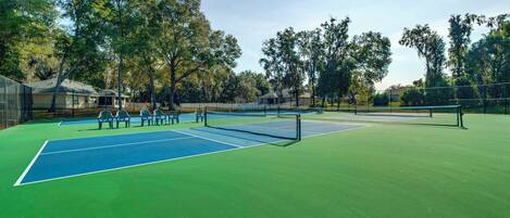 Ein Tennisplatz mit Netz, umgeben von Bäumen und einem Zaun.