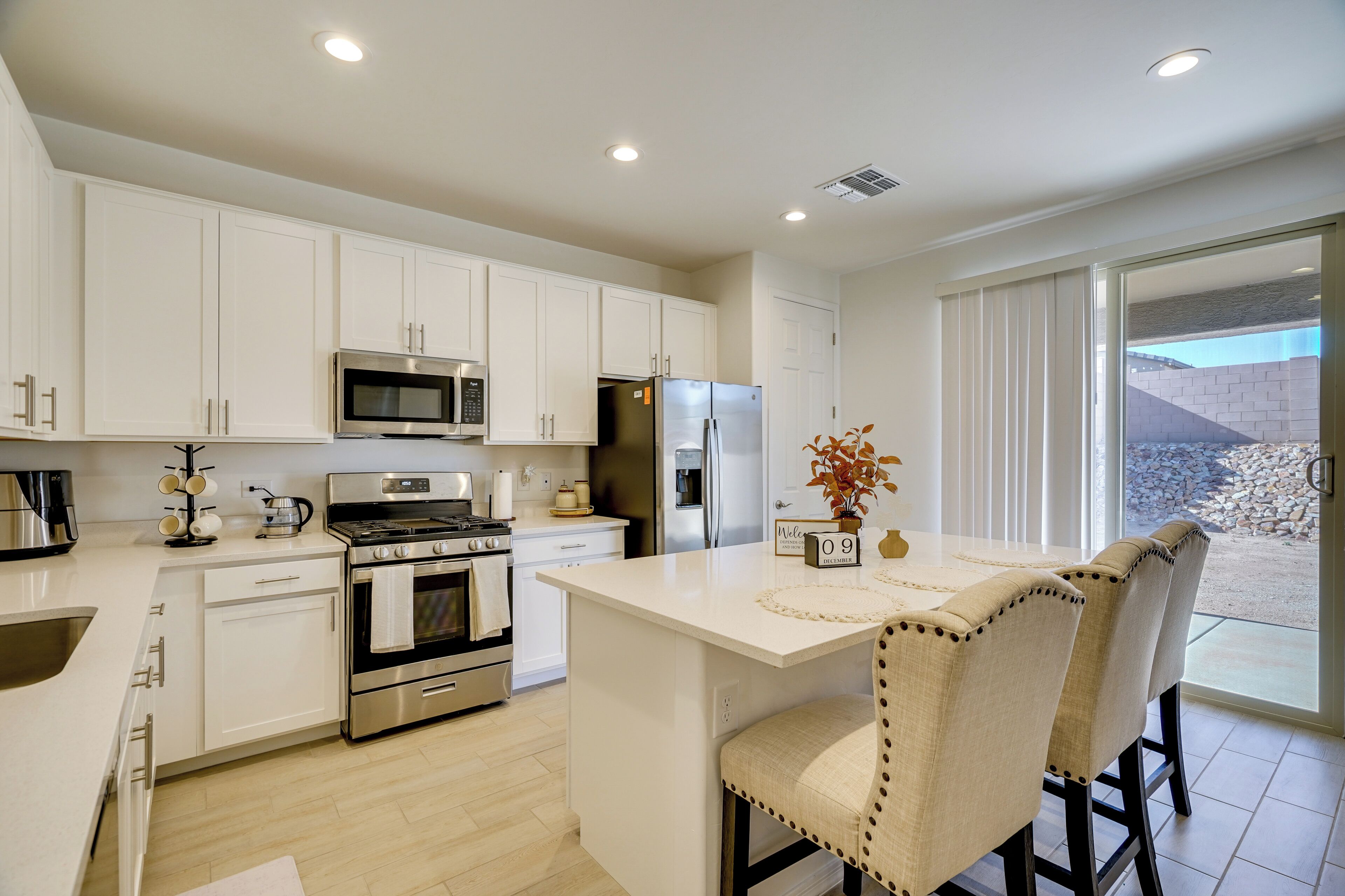 A modern kitchen with white cabinetry, stainless steel appliances, and a central island with chairs.