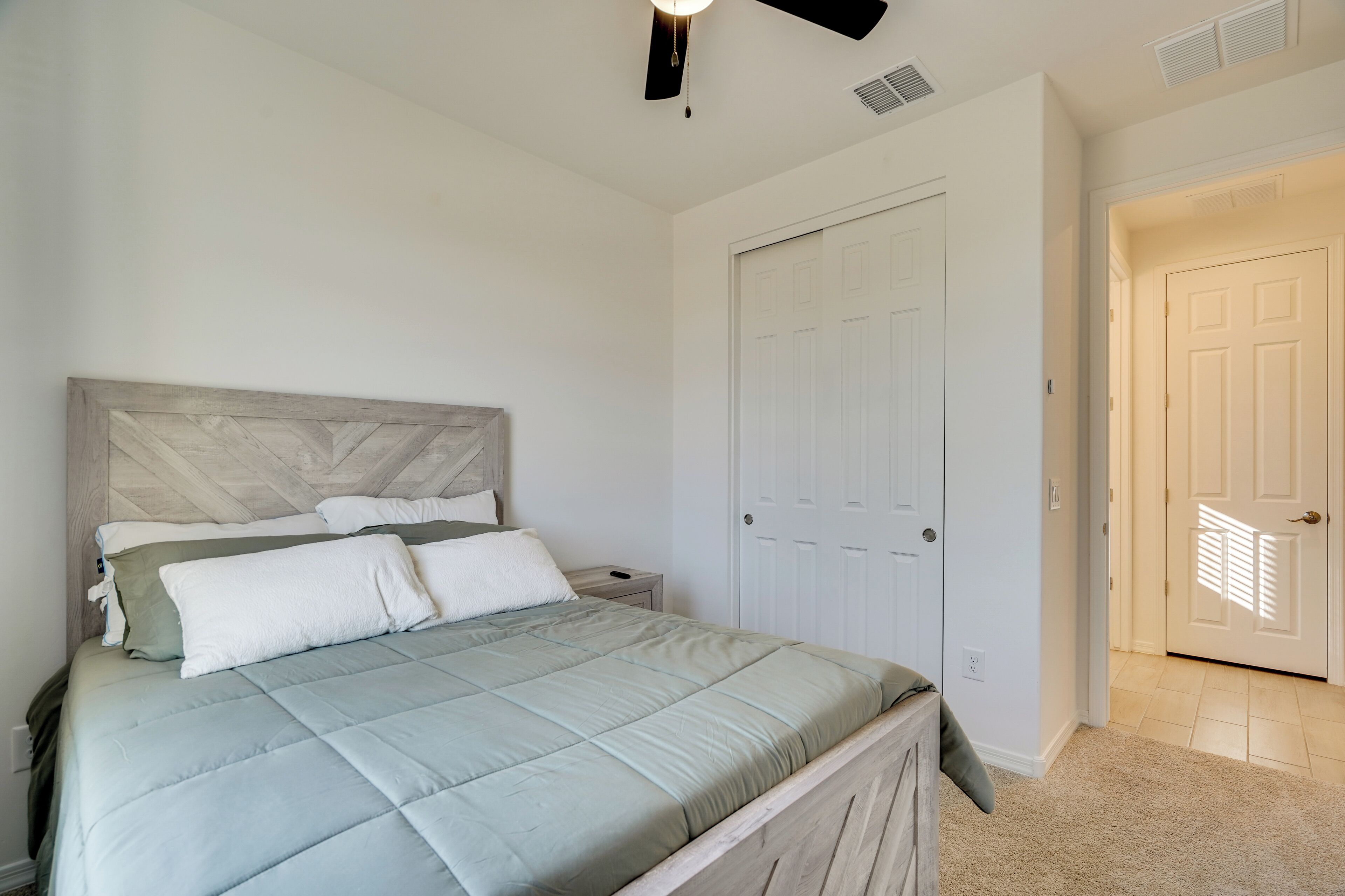 A bedroom with a bed, a nightstand, a door, and a carpeted floor.