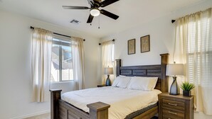 Un dormitorio con una cama de madera, dos mesitas de noche con lámparas, un ventilador de techo y una ventana con cortinas.
