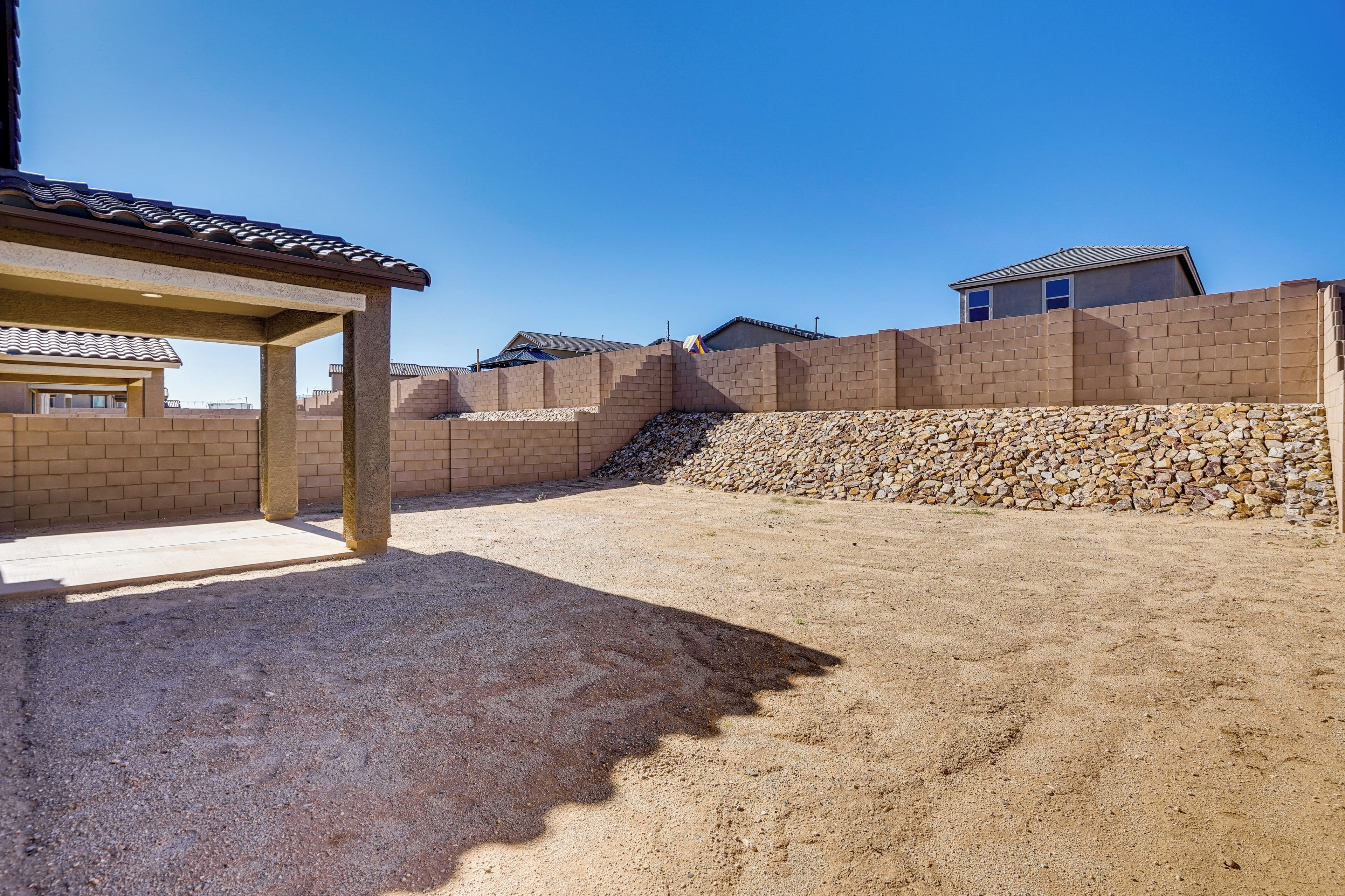 Zona residencial con un porche cubierto, un muro de contención de piedra y casas al fondo.