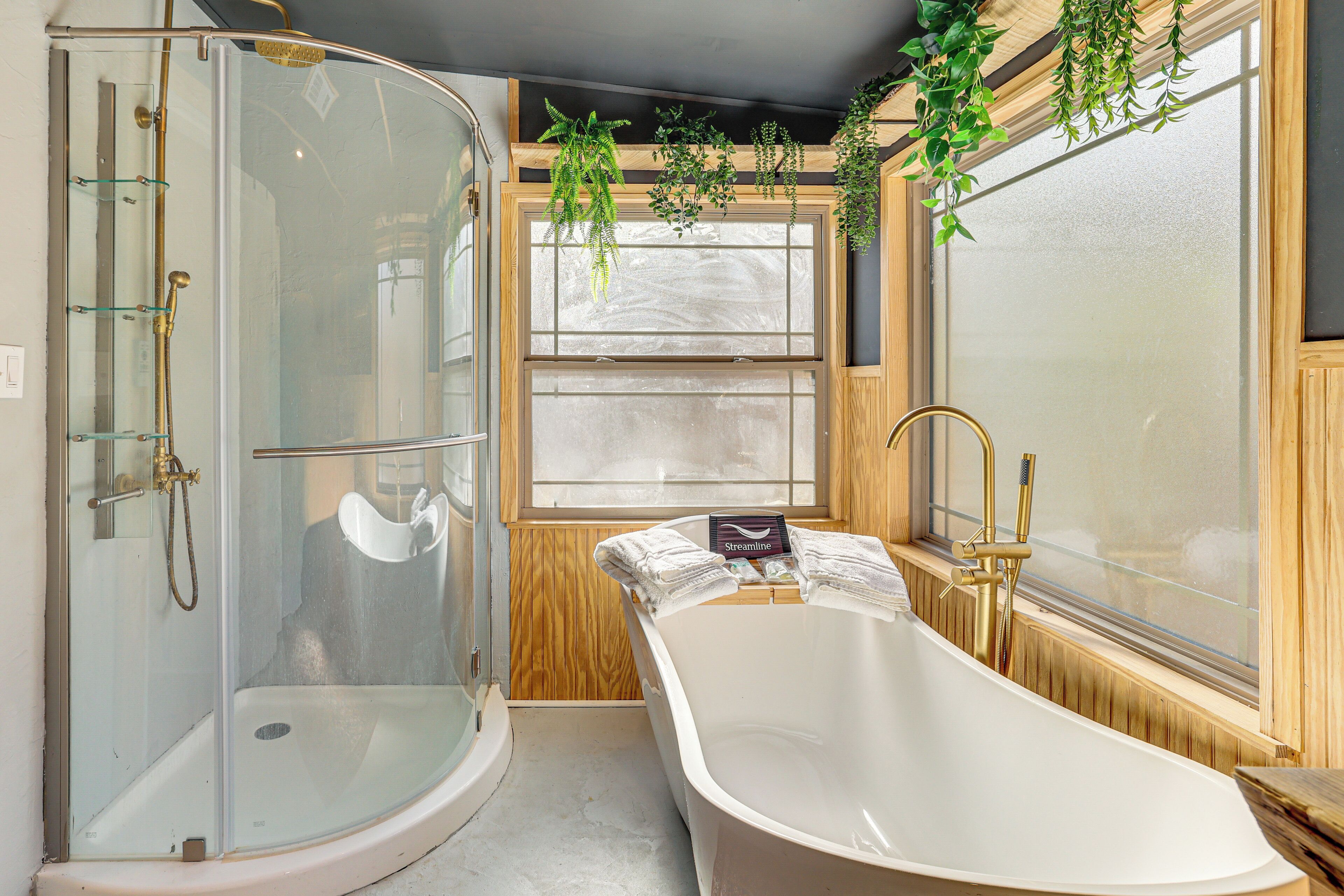 Un baño con ducha envuelta en vidrio, una bañera independiente y paneles de madera.