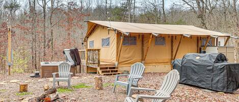 A tented campsite with a covered grill, two Adirondack chairs, and a fire pit.