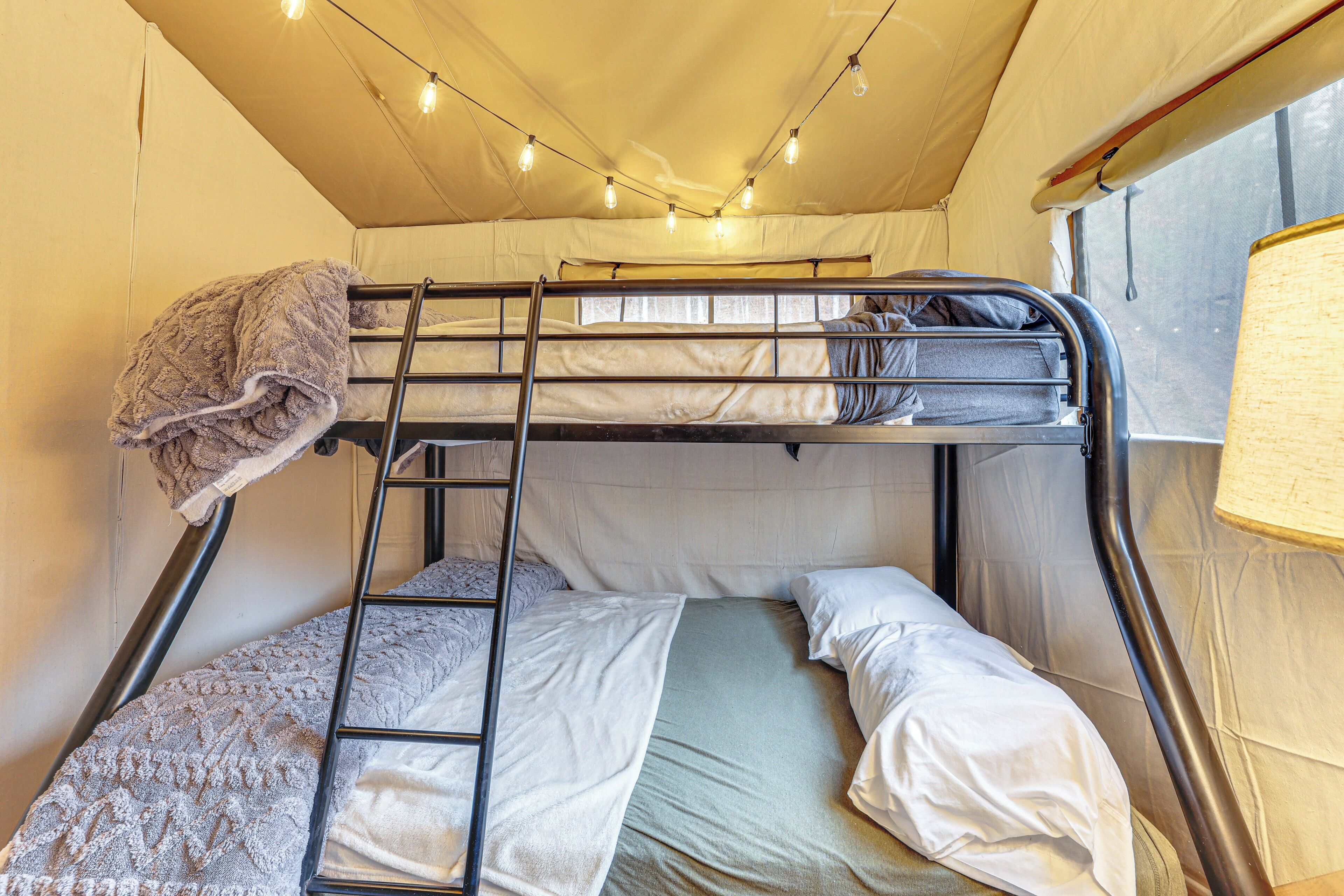 Un lit superposé avec une échelle, une couverture et une lampe.
