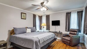 Une chambre à coucher comprenant un lit, un ventilateur de plafond, un bureau, une chaise et un téléviseur.