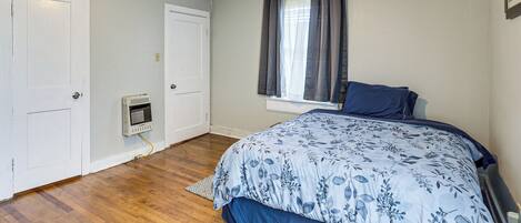 Un dormitorio con cama, un calentador, una ventana con cortinas y una puerta.