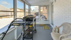 Een overdekte veranda met een grillwagen, een stoel en uitzicht op een achtertuin.