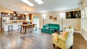 A spacious living area with a kitchen, a green sofa, and a television mounted on the wall. - Puget Sound Single-level Gem w/ Outdoor Fun! (Puyallup)