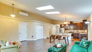 A spacious living area with a green sofa, a green ottoman, and a dining table with chairs. There is a kitchen area with dark wooden cabinets and a microwave. - Puget Sound Single-level Gem w/ Outdoor Fun! (Puyallup)