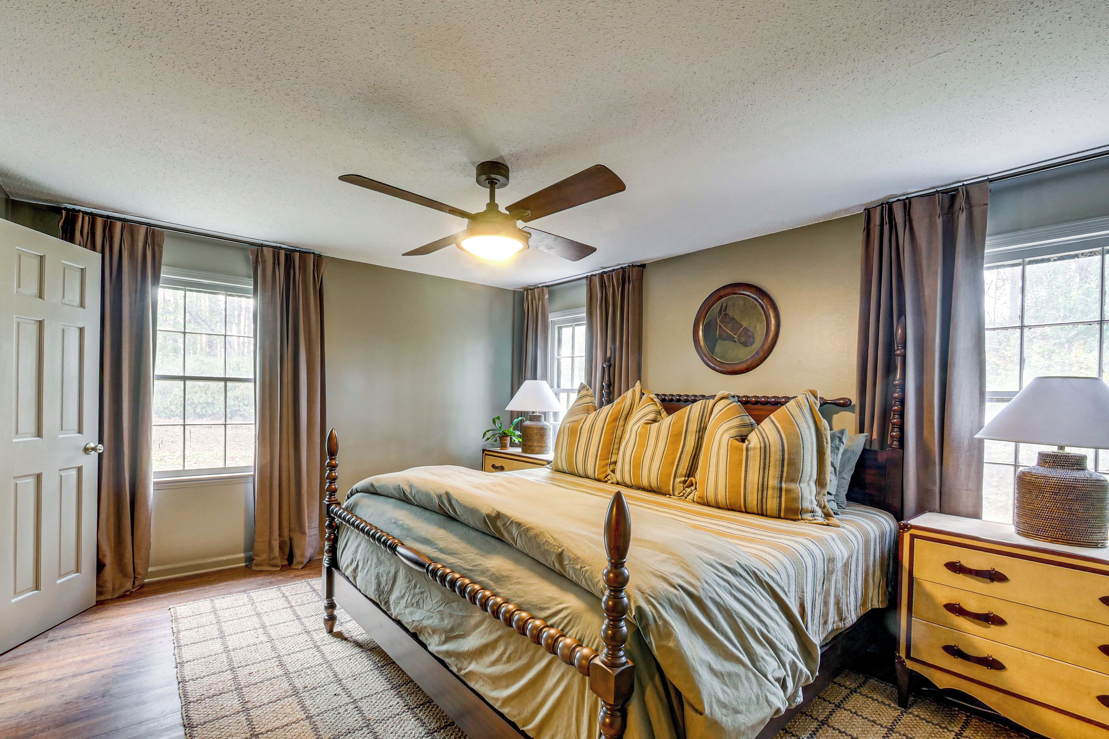 A bedroom with a bed, a nightstand, a lamp, a ceiling fan, and a window with curtains.