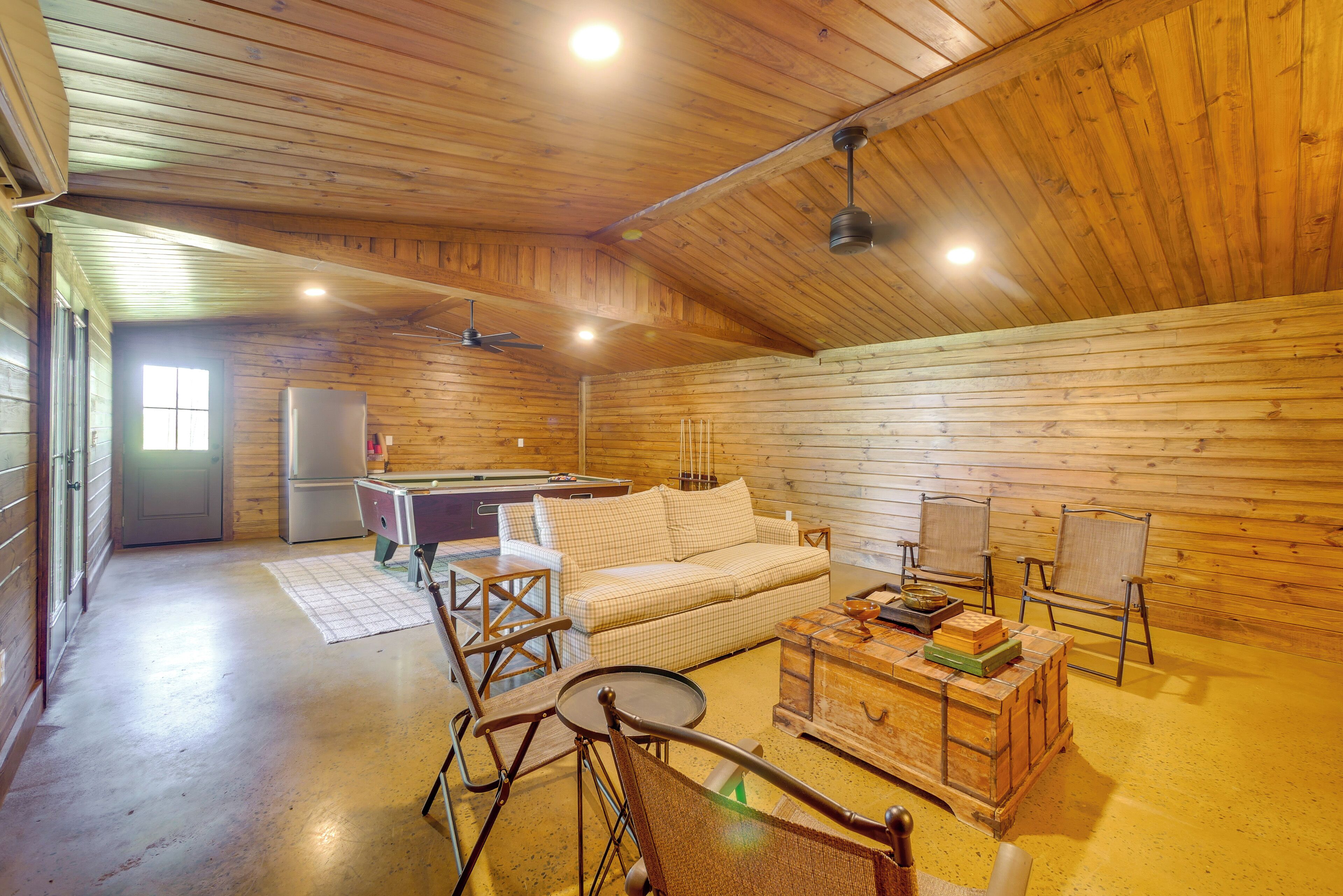 L’intérieur d’une cabane en rondins, avec un plafond en bois, un canapé, une table basse, une table à manger et un réfrigérateur.