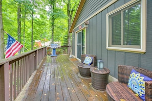 A wooden deck with wicker furniture, an American flag, and a building with a large window. - Crystal Mountain Cabin: Fall Views, Golf, Ski (Thompsonville)