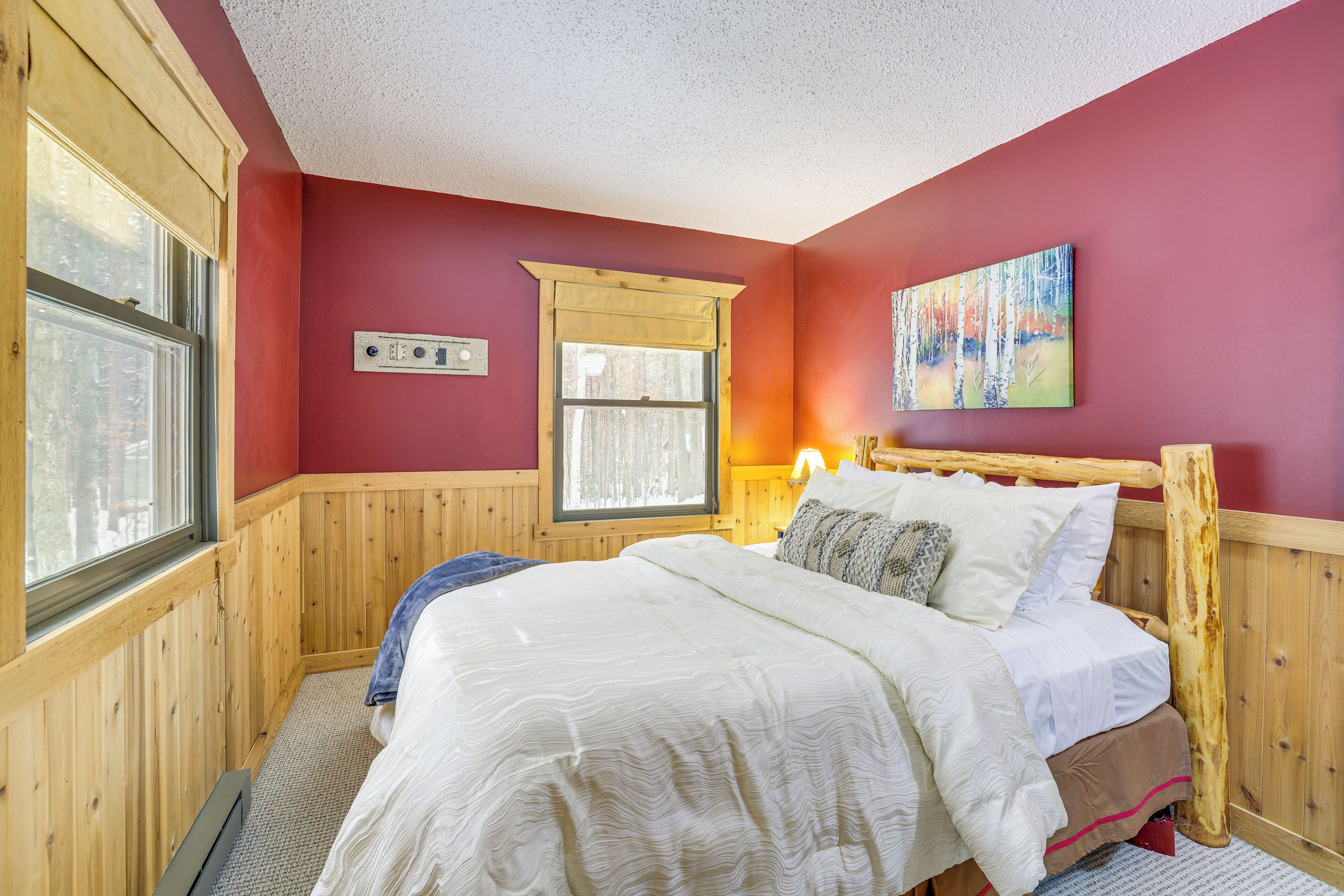 A cozy bedroom with a wooden bed, a window with a view, and a painting on the wall.