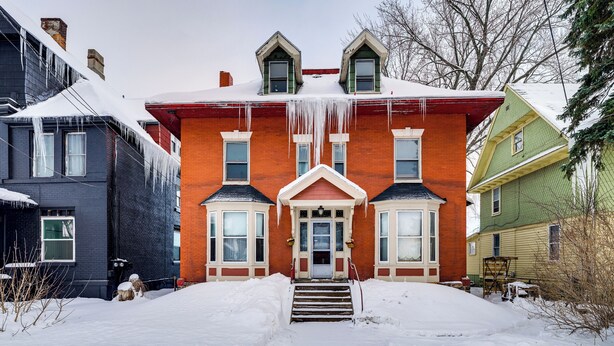 Una casa a due piani in mattoni con una porta rossa e decorazioni bianche, circondata dalla neve.