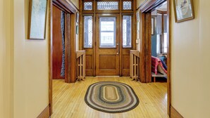 Un corridoio con pavimento in legno, un tappeto decorato e una porta in legno con vetri, con opere d'arte incorniciate alle pareti.