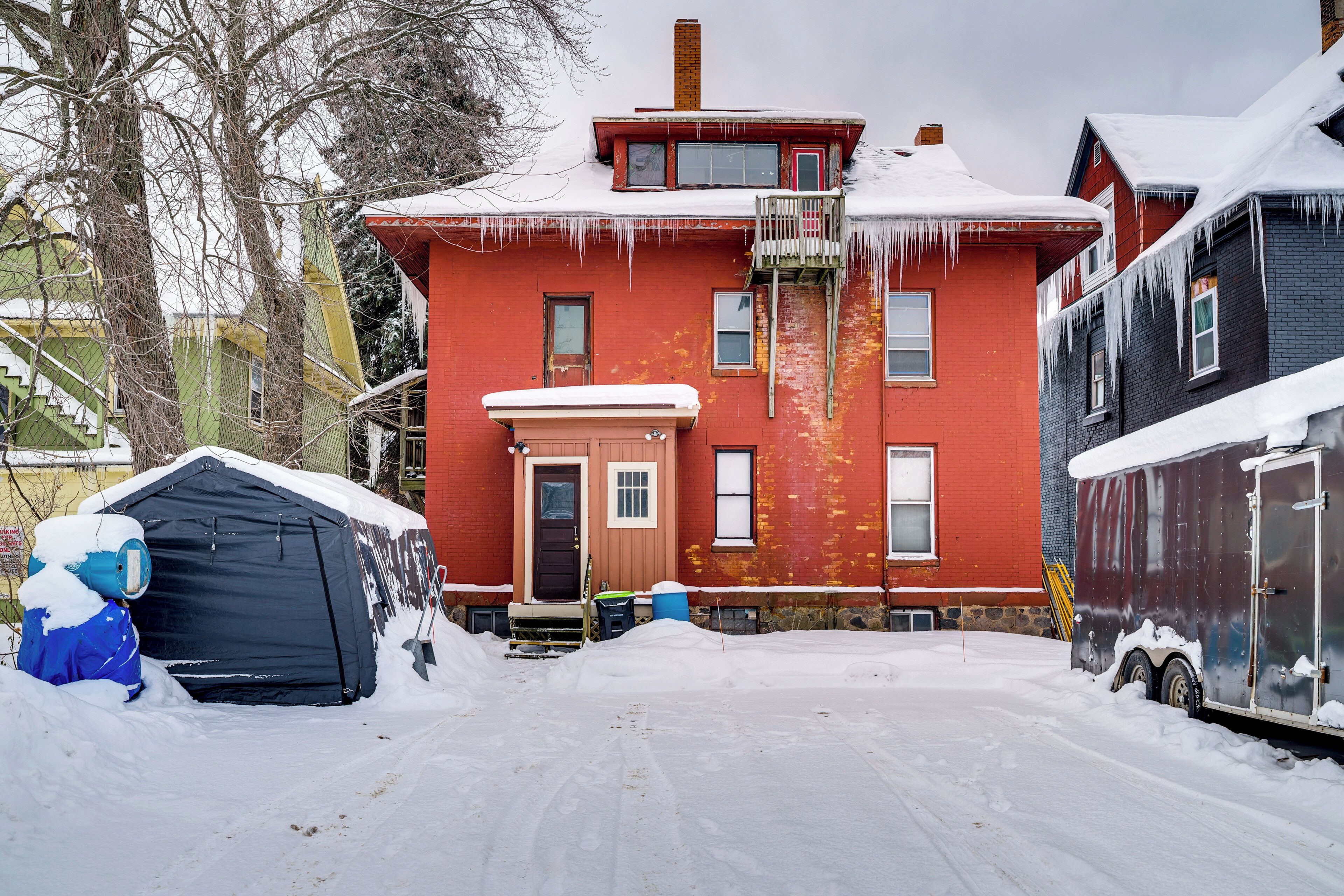 Una casa roja con un garaje negro y una tienda de campaña azul en la nieve.