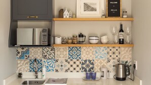 A kitchen with a microwave, coffee maker, and kettle on the counter. There are shelves above with decorative items and a framed picture. - SurfWay beach cottage - Your Cape beach getaway (Cape Town)