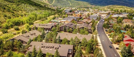 An aerial view of a town with a main road, buildings, and surrounding greenery.