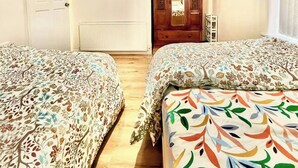 A room with two beds, a wooden wardrobe, a radiator, and a door with a mirror. - 3bedroom Entire House in Stockport Town Manchester (Stockport)