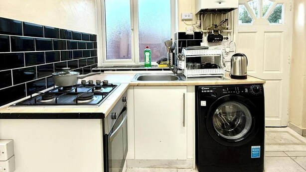 A compact kitchen with a gas stove, a washing machine, and a window with a view of trees. - 3bedroom Entire House in Stockport Town Manchester (Stockport)