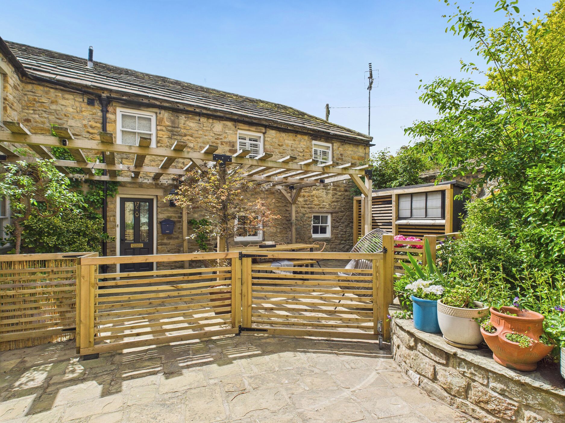A stone house with a wooden gate, a covered patio, and potted plants.