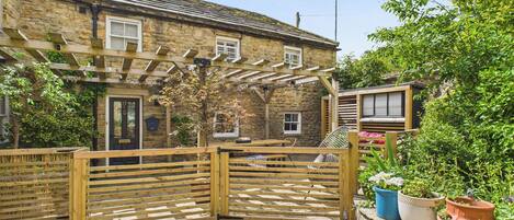 A stone house with a wooden gate, a covered patio, and potted plants.
