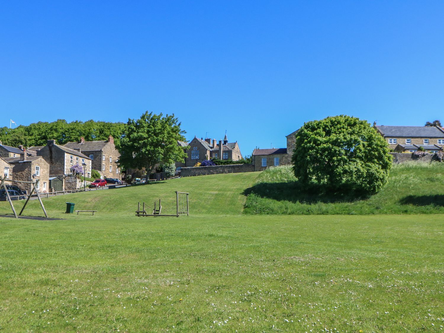 A grassy field with a swing set, a stone building, and a large tree.