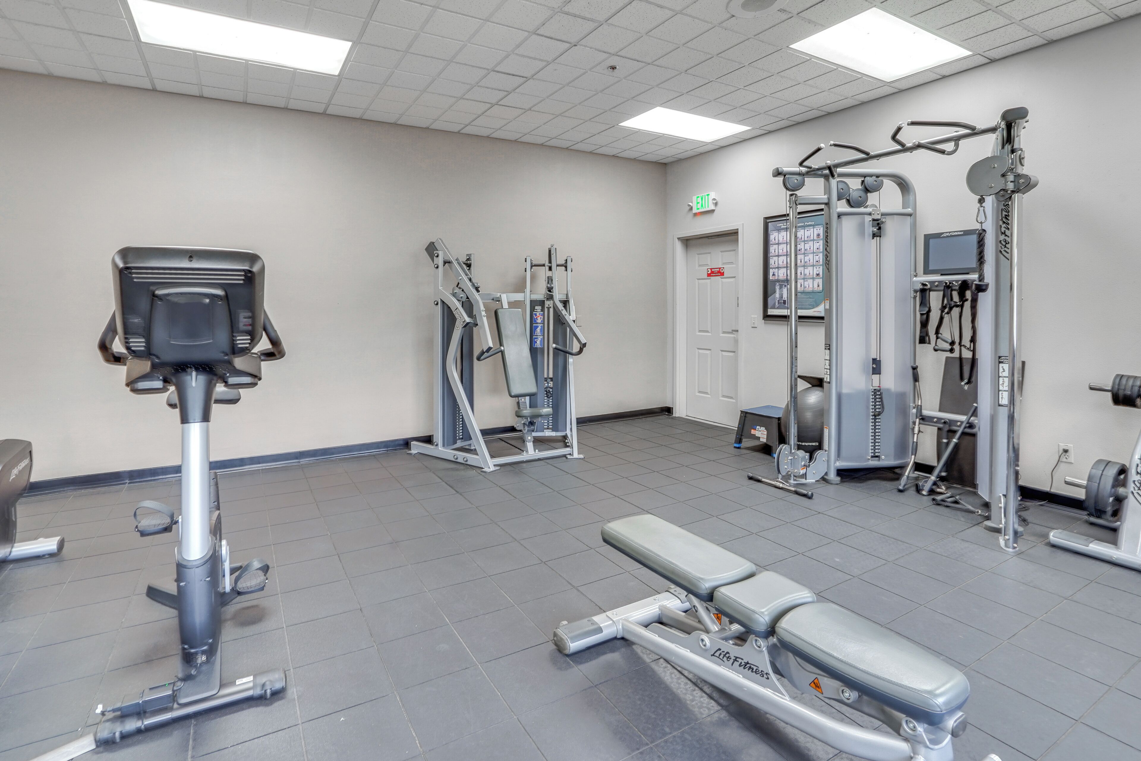 Een sportschool met diverse fitnessapparatuur, waaronder een hometrainer, krachttoestellen en een bank.