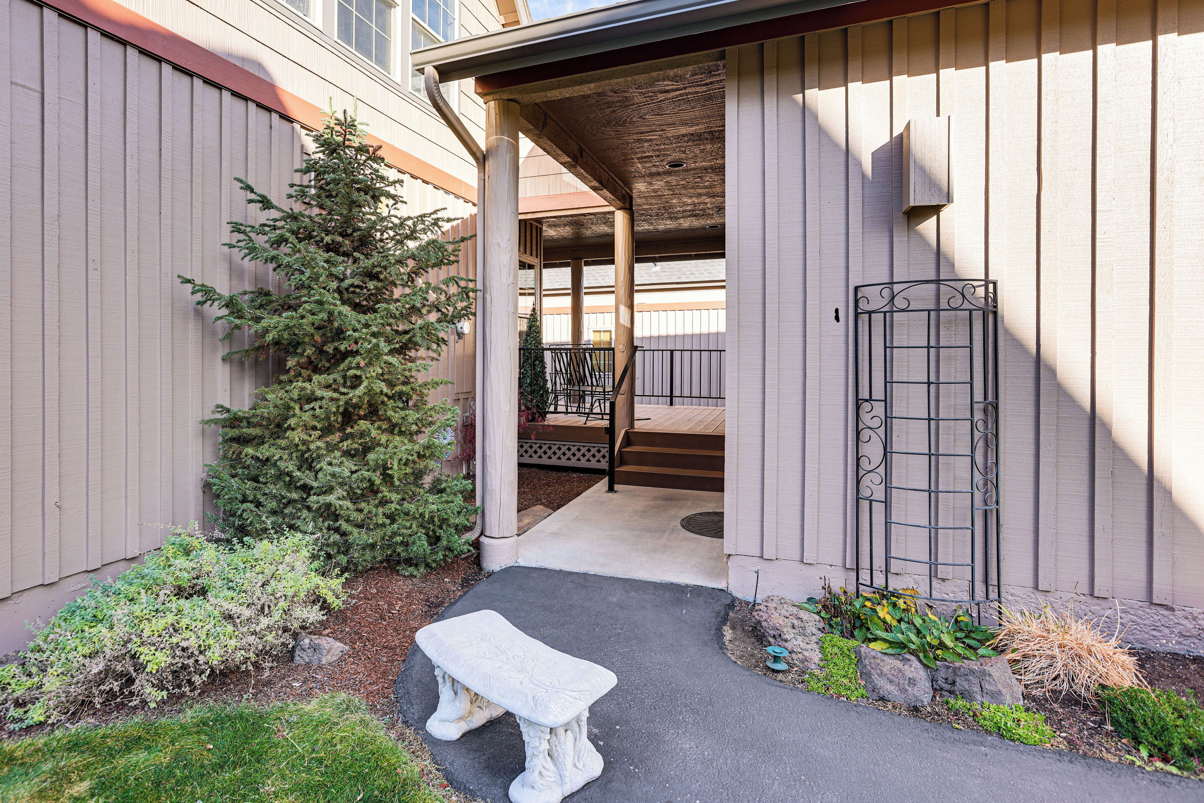 A covered patio area with a stone bench, a small tree, and a metal gate.