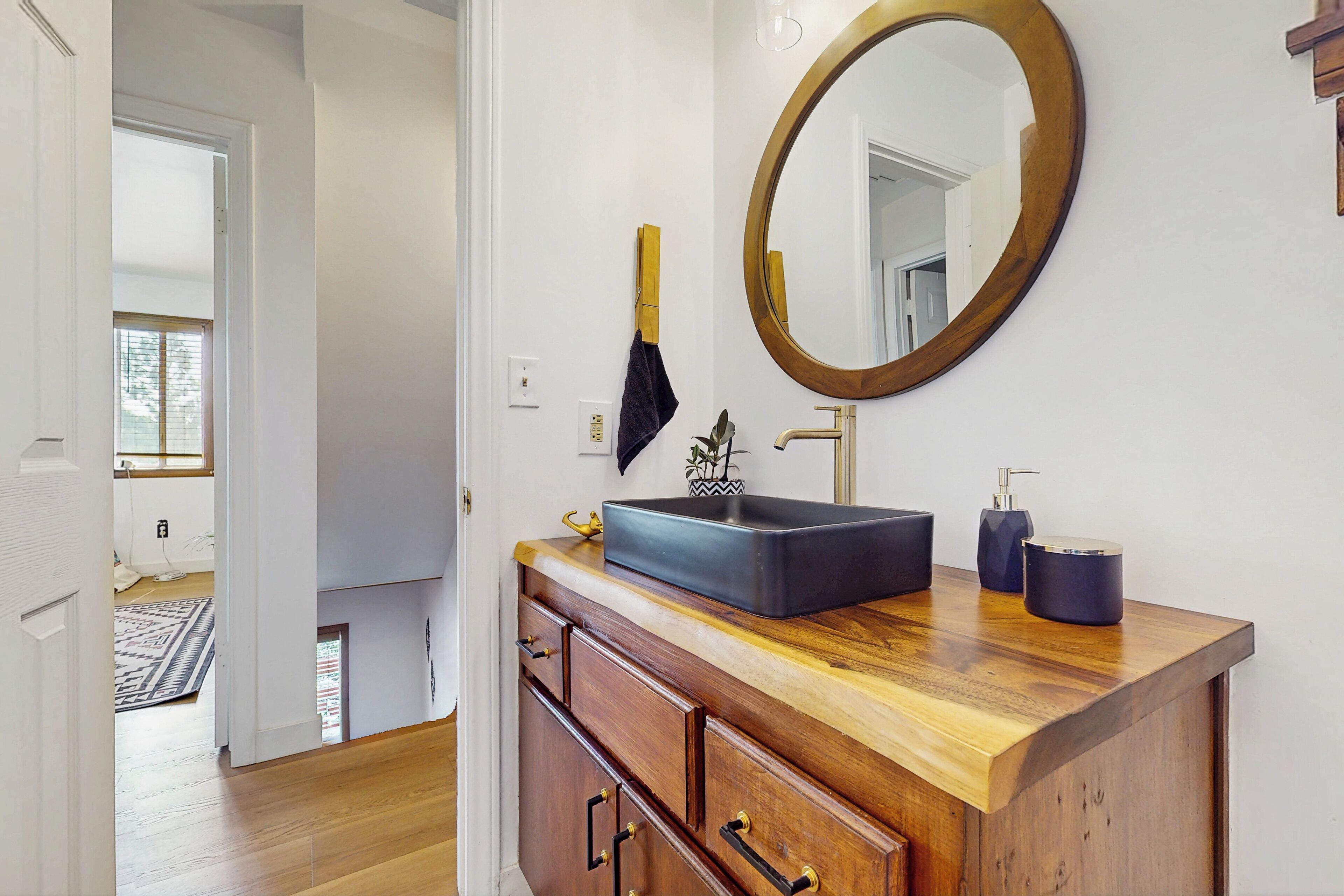 A bathroom with a wooden vanity, a round mirror, and a black sink.