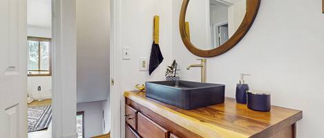 A bathroom with a wooden vanity, a round mirror, and a black sink.