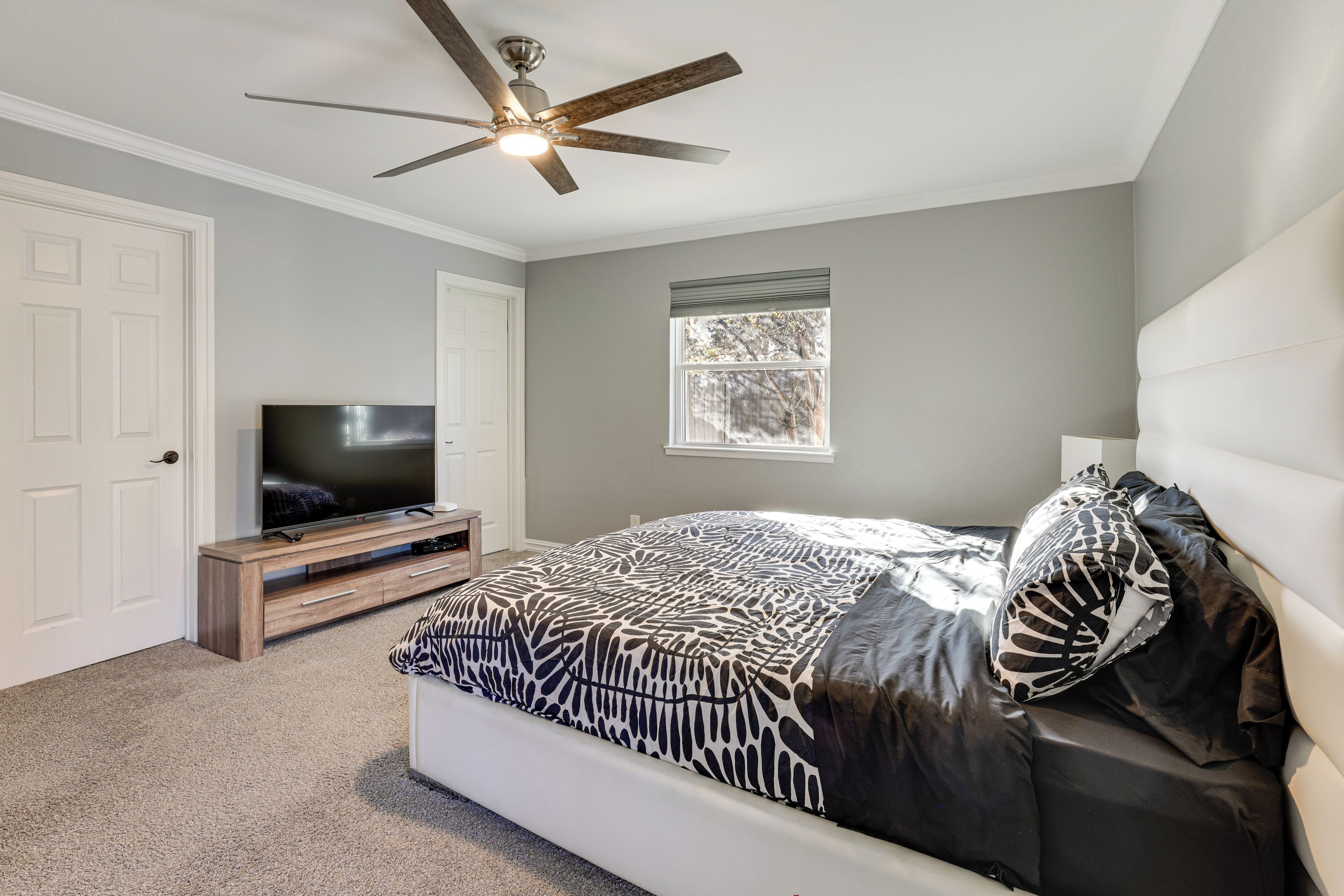 A bedroom with a bed, a TV, a ceiling fan, and a window.