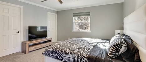 A bedroom with a bed, a TV, a ceiling fan, and a window.