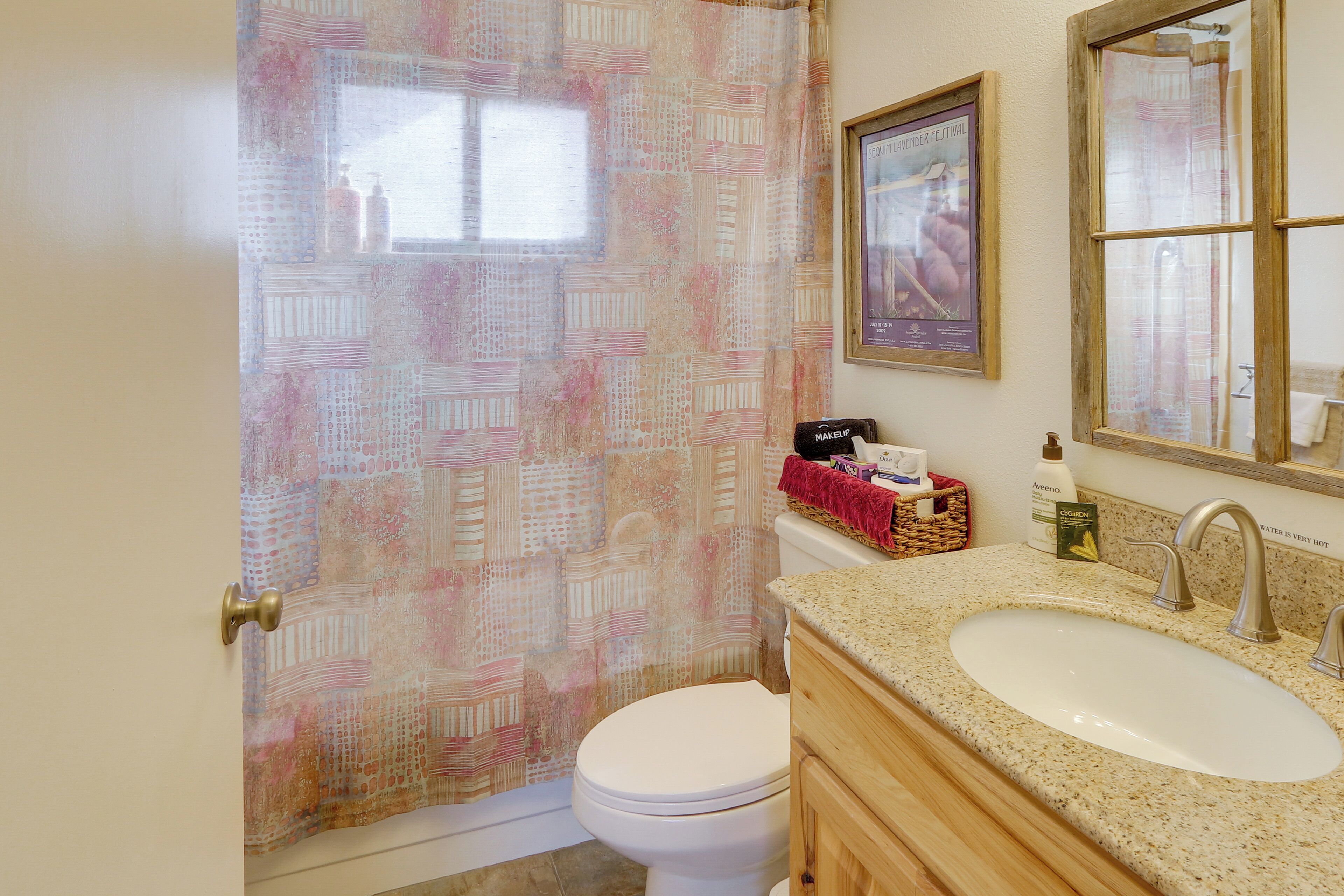 Un baño con cortina de ducha estampada, un inodoro, un lavabo con espejo y artículos de aseo en la encimera.