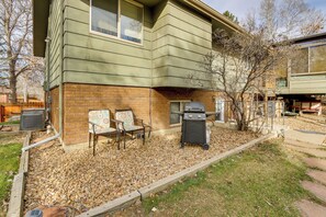 A house with a brick foundation and green siding, a patio with two chairs, a grill, and a tree. - 6 Mi to Dtwn Fort Collins: Cozy Apt w/ Shared Yard (Fort Collins)