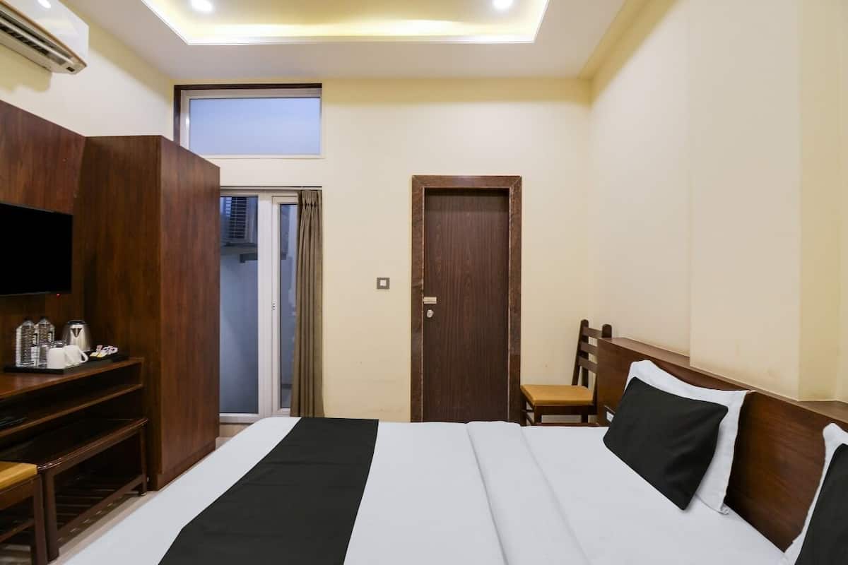 A hotel room with a bed, a wooden wardrobe, a television, a chair, and a door.