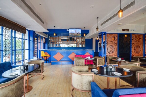 A modern restaurant with blue and orange decor, multiple seating areas, and a TV screen on the wall. - Hotel Maanvad Garh by Keshav Residency (Udaipur)
